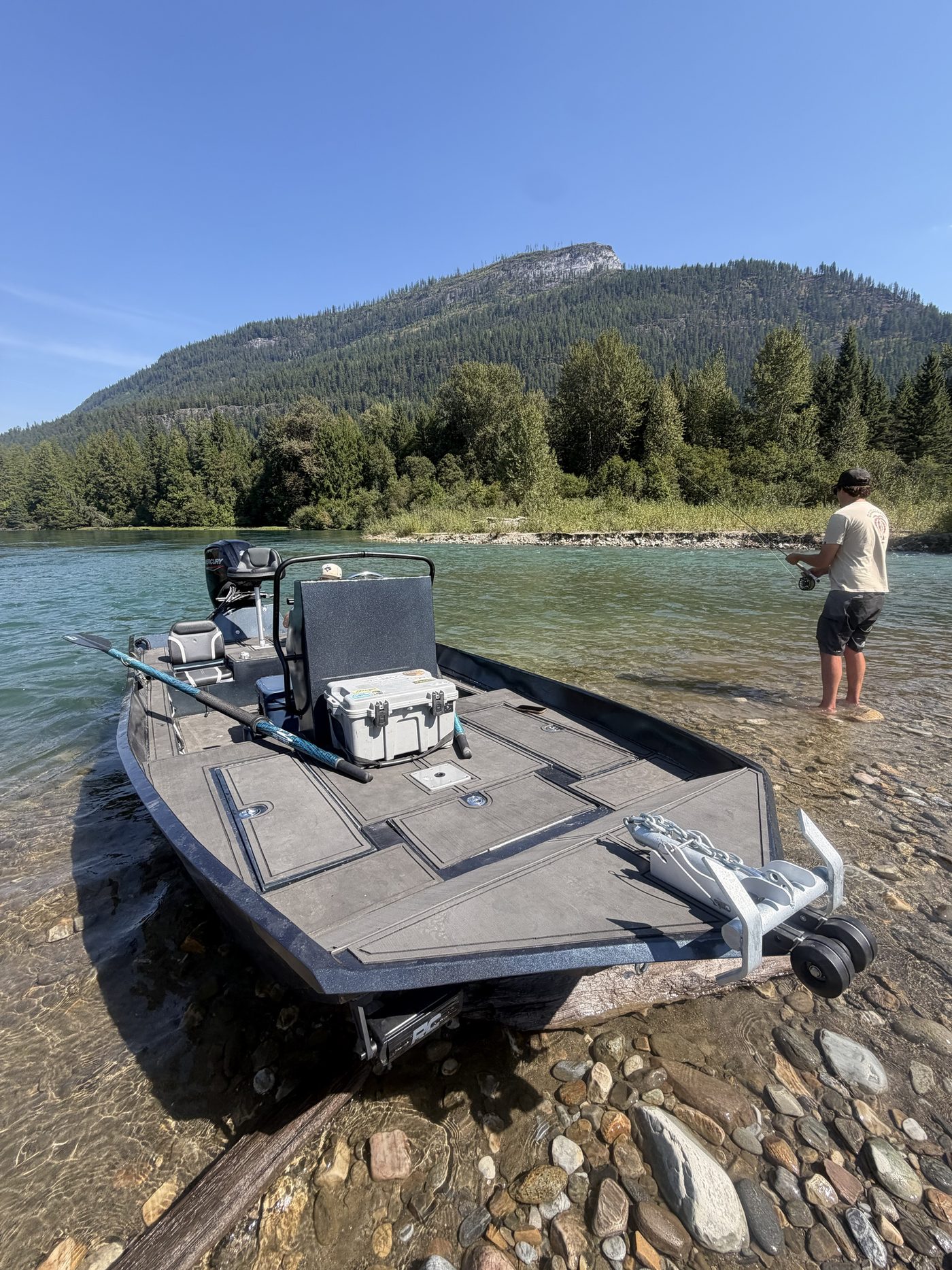 An Unreel jet boat nosed up on a gravel bar in a clear BC river while an angler casts nearby